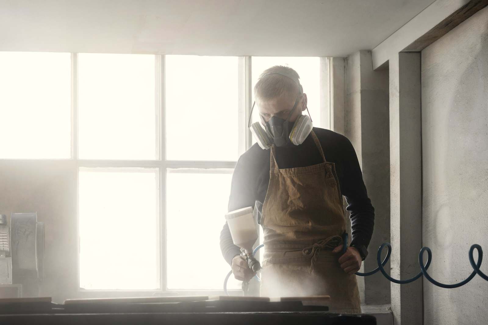 A maker in an apron working by a bright workshop window